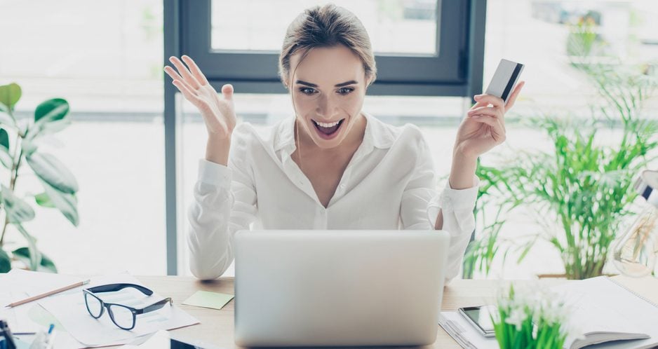 Woman holding a credit card in her hand and looking happily surprised at her laptop