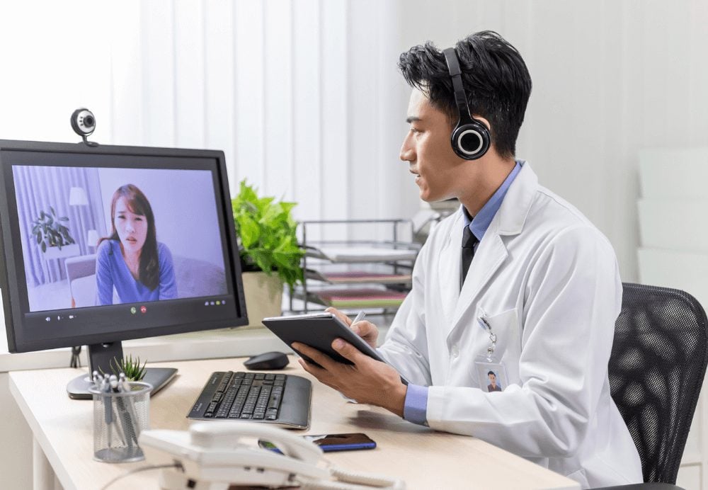 Chiropractors_Telemedicine concept - asian male doctor has video call with female patient with depression online by webcam in clinic