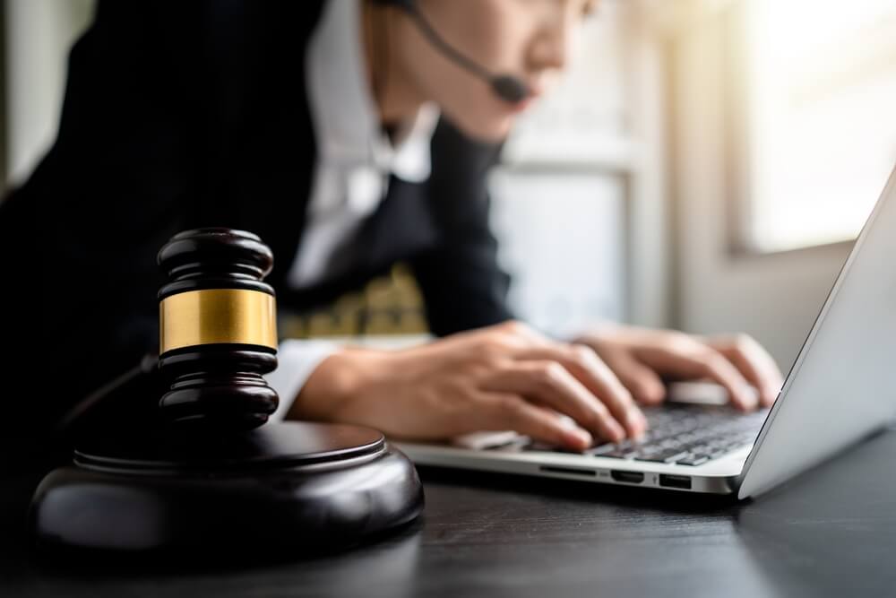 law firms_Close up of view gavel with female Lawyer or Business women wearing headset using laptop in the background at a law firm, selective focus, consult legal online, Justice and law concept.