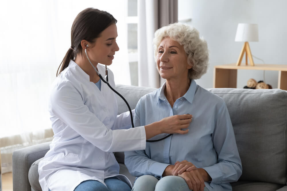 home health providers_Young woman nurse doctor gp holding stethoscope examining old senior 60s grandma patient check heartbeat at homecare checkup medical visit at home hospital, older people cardiology healthcare concept