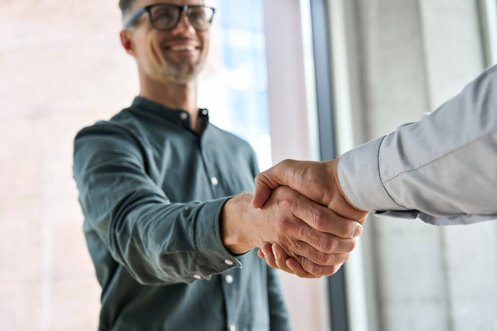 influencers_collaboration_Two happy diverse professional business men executive leaders shaking hands at office meeting. Smiling businessman standing greeting partner with handshake. Leadership, trust, partnership concept.