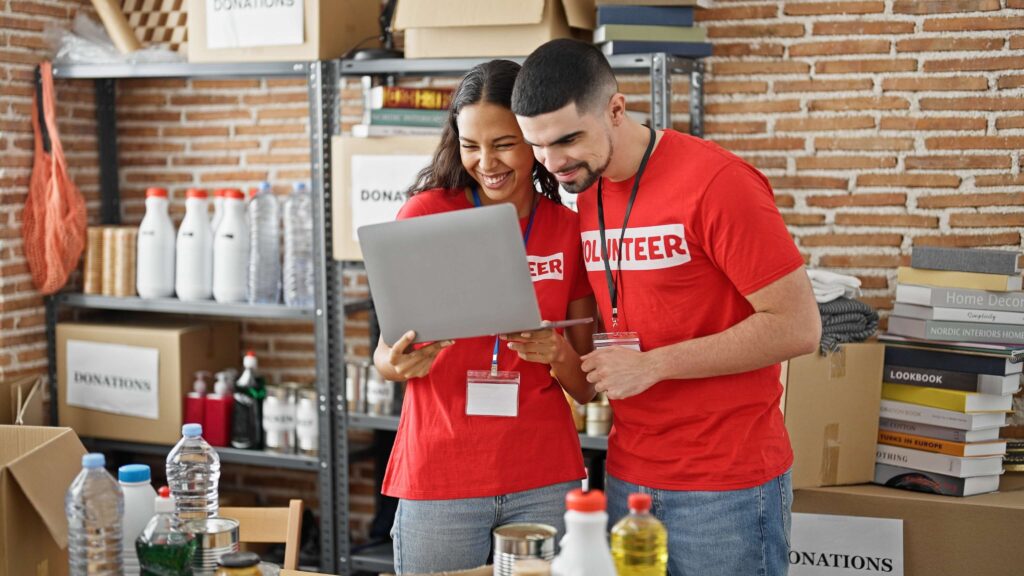 Surrounded by donations, 2 people in red shirts that say "volunteer" look at a computer to see the email marketing for nonprofits guide