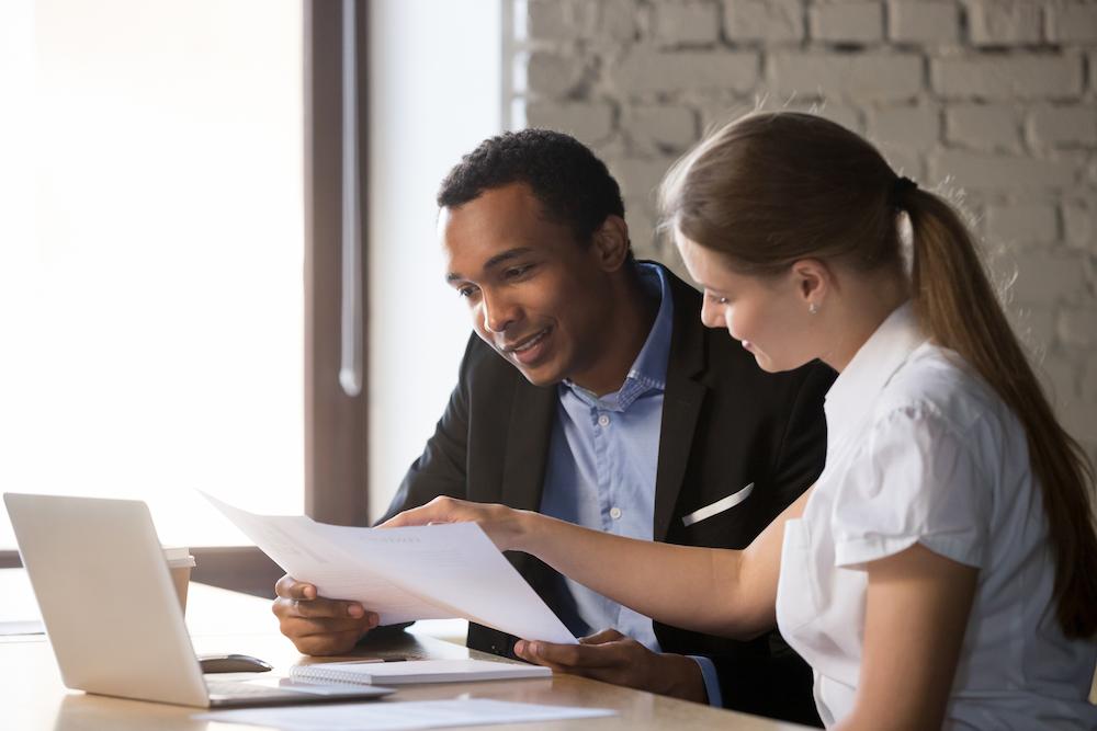 A virtual compliance officer presents her client with an audit of his company at a desk with a laptop and papers