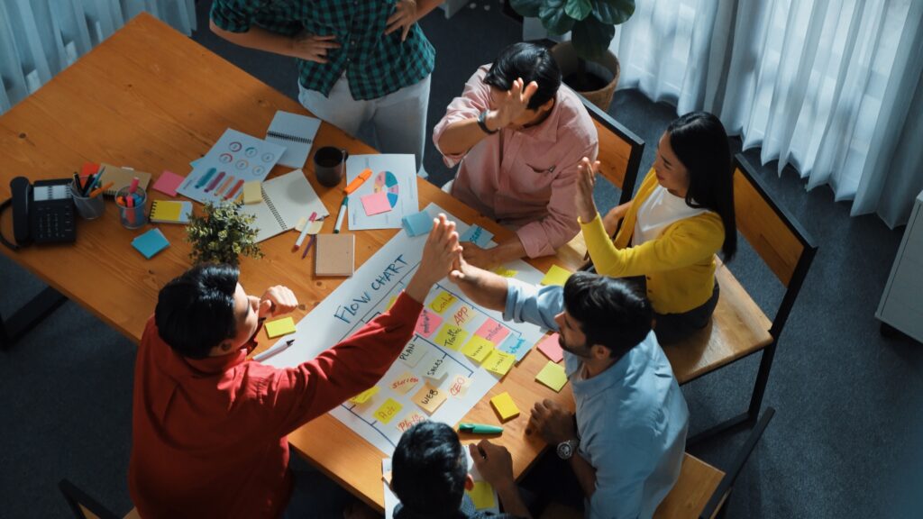 Group of businesspeople around a conference table high-five each other after talking about the reasons to hire a New York FCMO 