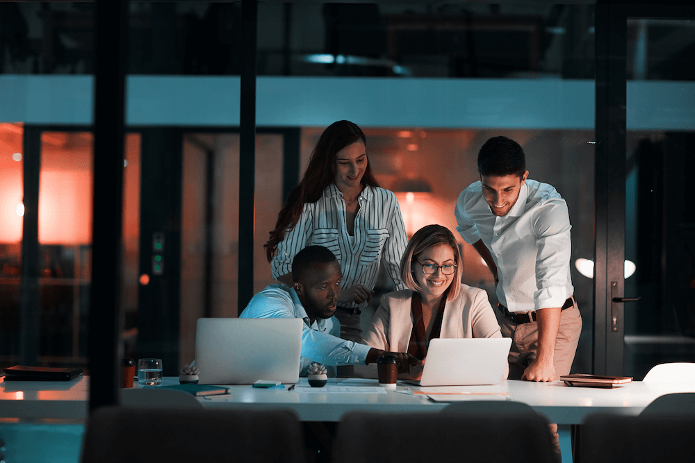 Four marketers look over a fractional marketing director's presentation on a laptop in an office at evening