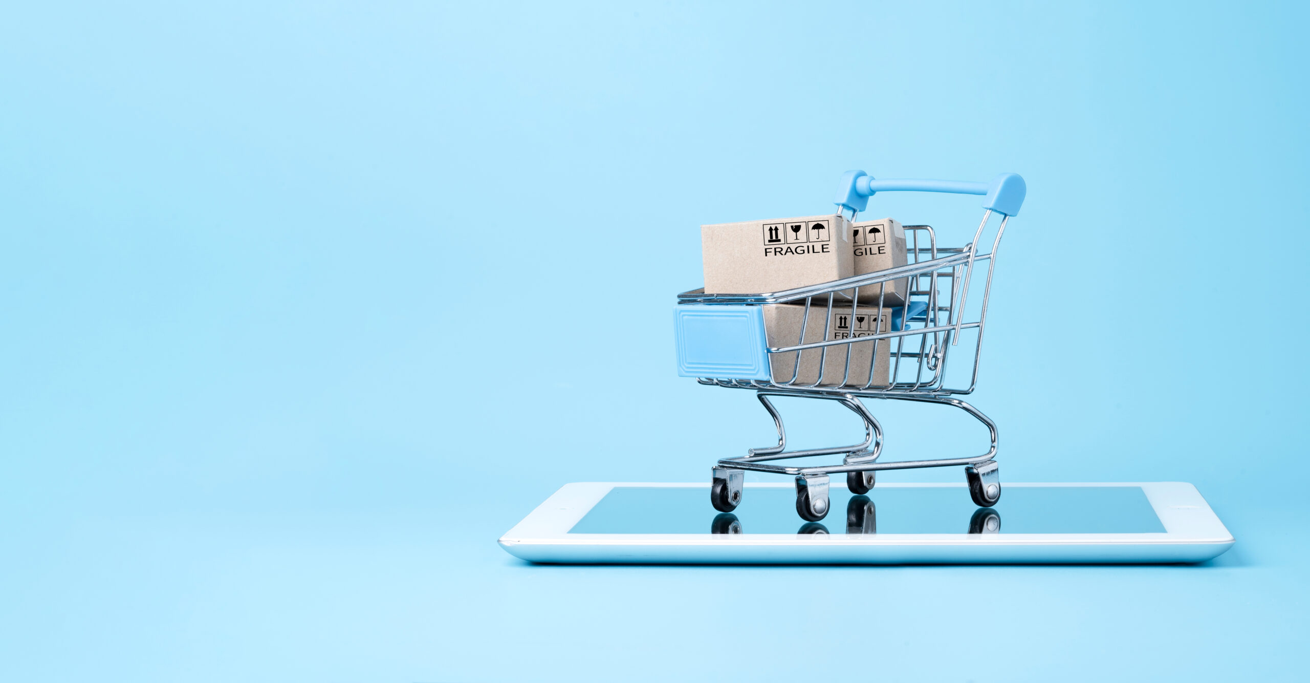 A mini shopping cart filled with boxes on a tablet with a blue background