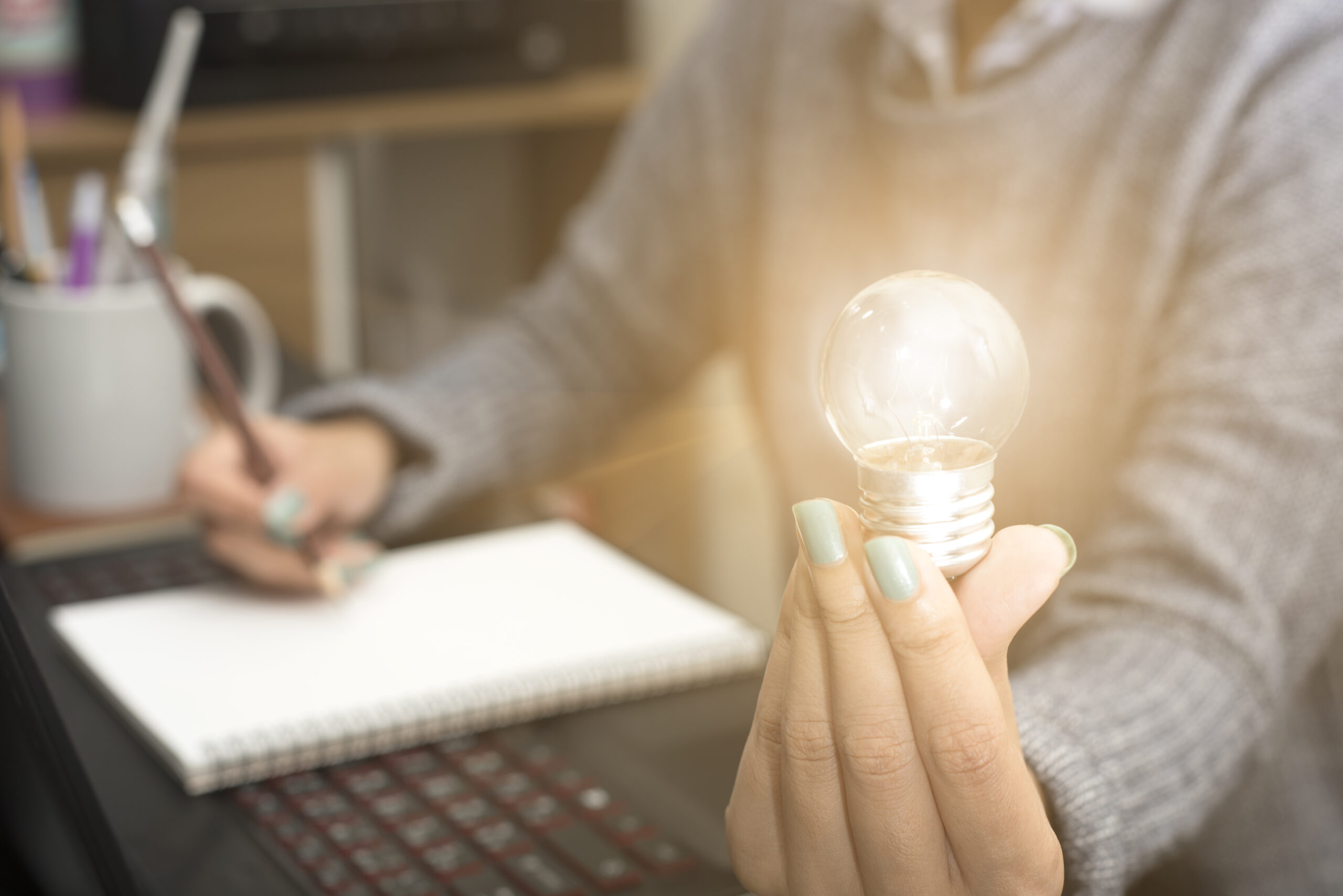 A businesswoman holds a lightbulb and a pen while working on marketing for Austin Entrepreneurs